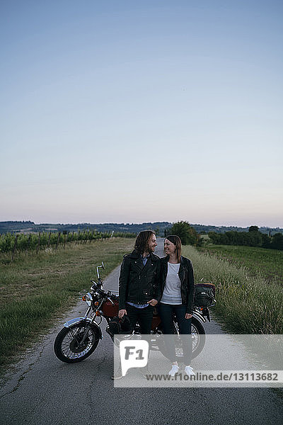 Junges Paar steht sich mit dem Motorrad gegen den klaren Himmel auf der Landstraße gegenüber