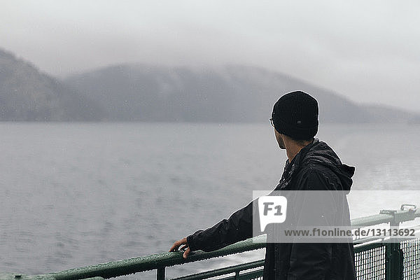 Mann betrachtet Aussicht  während er an der Reling eines Kreuzfahrtschiffes steht