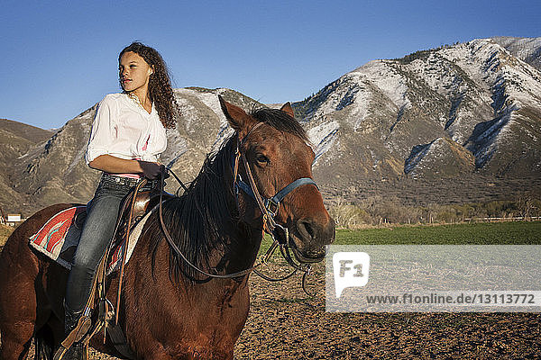 Female teenager looking away while sitting on horseback against mountains