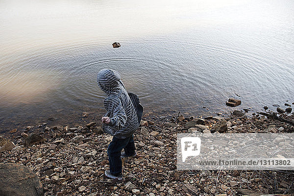 Seitenansicht eines Jungen mit Kapuzenhemd  der einen Stein in den See wirft