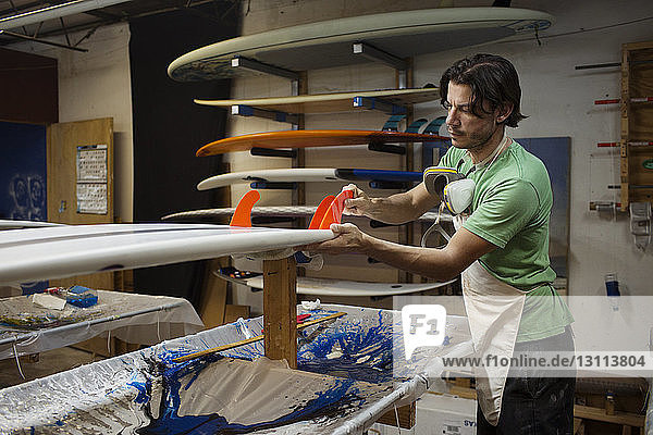 Konzentrierter Arbeiter stellt in der Werkstatt ein Surfbrett her