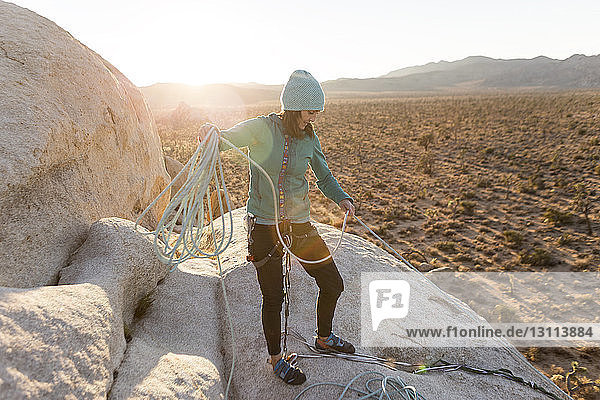 Wanderer  der bei Sonnenuntergang am Berg steht und sein Seil verstellt