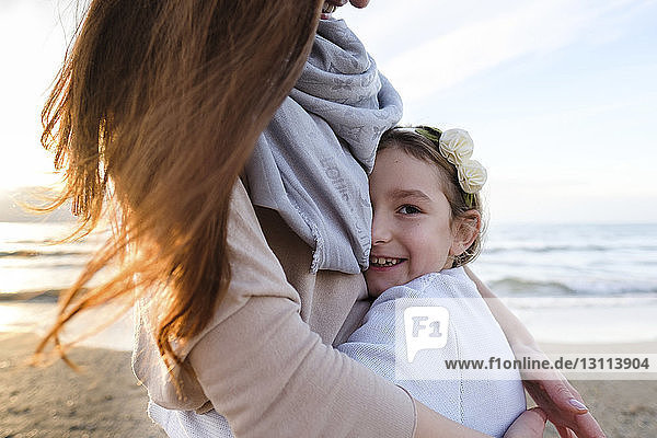 Porträt einer glücklichen Tochter  die ihre Mutter umarmt  während sie bei Sonnenuntergang am Strand steht
