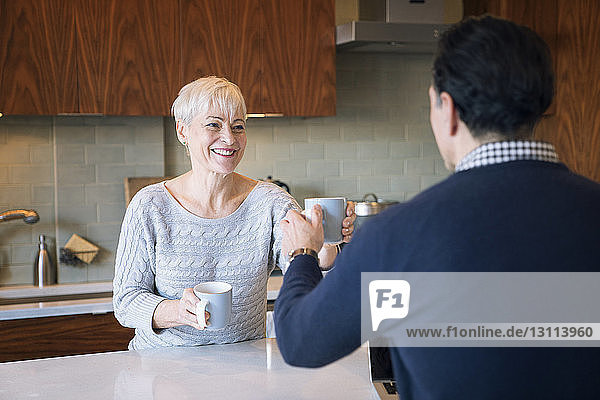 Lächelnde Frau überreicht Mann einen Becher  während sie zu Hause am Tisch sitzt