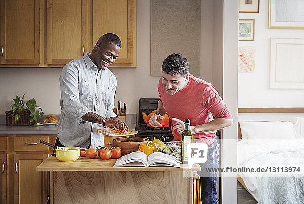 Happy multi-ethnic gay couple preparing food in kitchen at home