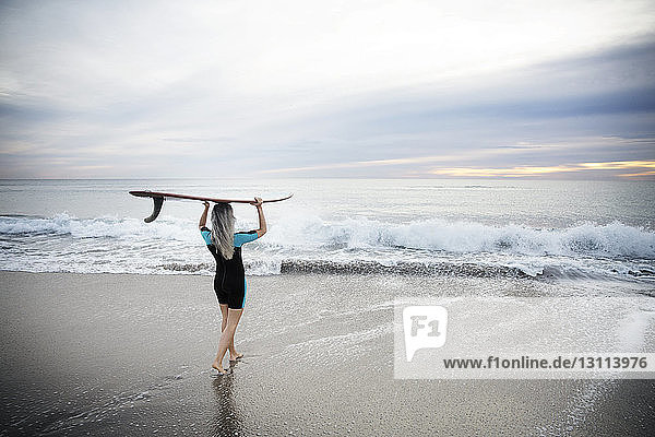 Rückansicht einer Surferin  die ein Surfbrett auf dem Kopf trägt  während sie am Strand von Delray in Richtung Meer läuft