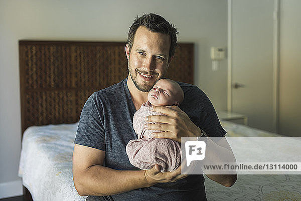 Porträt eines glücklichen Vaters  der seine neugeborene Tochter im Schlafzimmer trägt