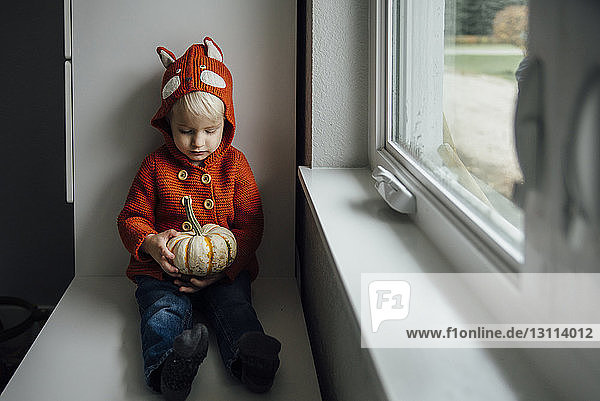 Süßer Junge schaut Kürbis an  während er zu Hause an Halloween am Fenster sitzt