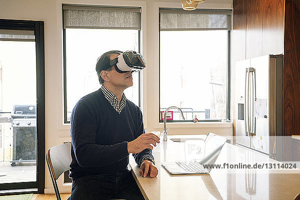 Man wearing virtual reality simulator sitting at table in kitchen