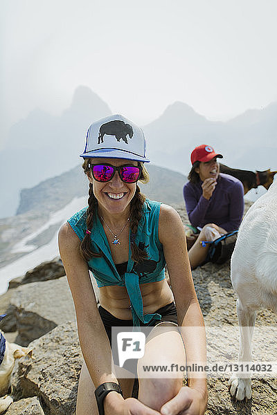 Female hikers with dog sitting on mountain against clear sky