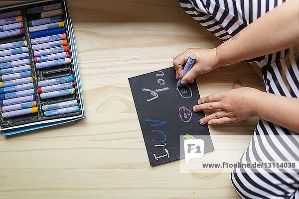 Mittelteil einer Mädchenzeichnung mit bunten Buntstiften auf Papier  während sie zu Hause kniet