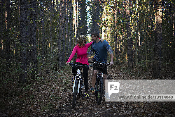 Couple mountain biking together against trees in forest