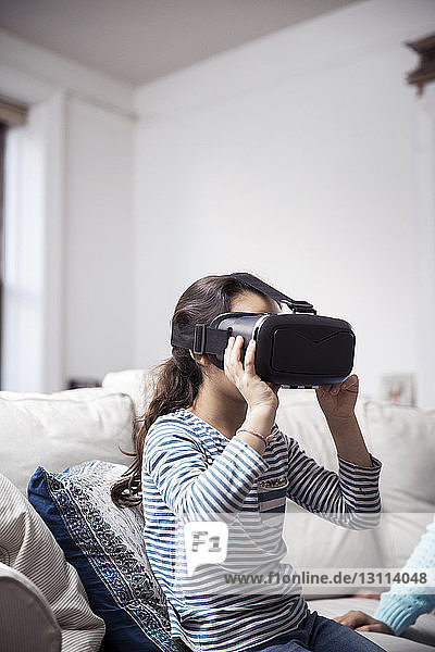 Girl using virtual reality simulator while sitting with sister at home