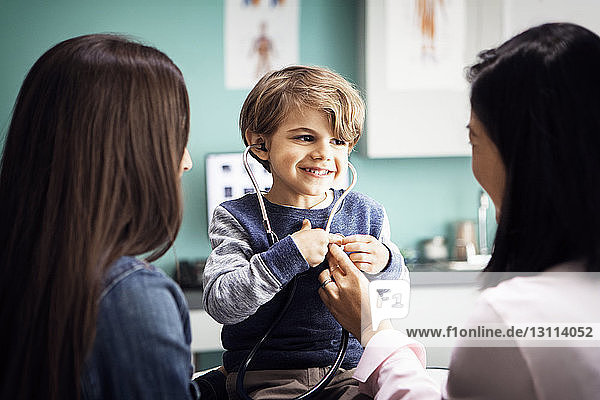 Cute boy listening to his heartbeat with female doctor and mother in clinic