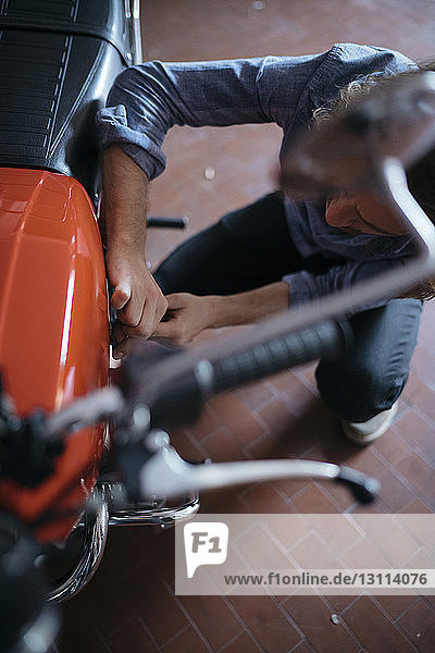 Hochwinkelaufnahme eines Mannes  der sein Motorrad in der Werkstatt repariert
