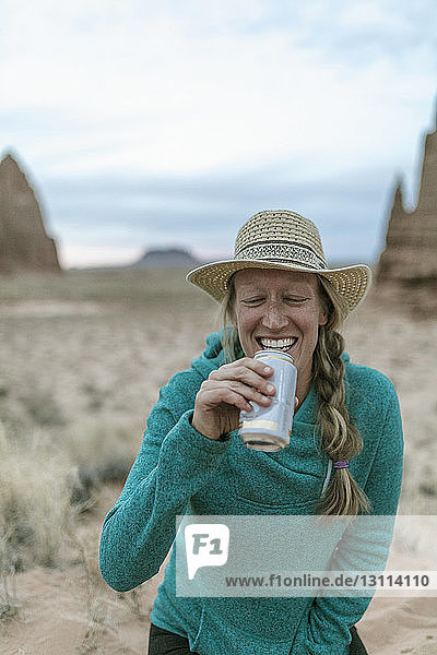 Fröhliche Wanderin mit Hut beim Trinken in der Wüste