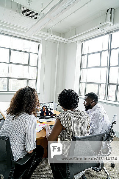 Geschäftsleute diskutieren mit Geschäftsfrau über Videokonferenz im Sitzungssaal im Büro