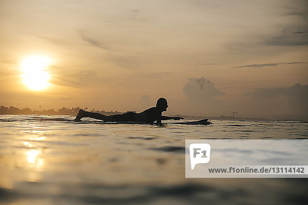 Seitenansicht der Silhouette eines Mannes  der bei Sonnenuntergang auf dem Meer gegen den Himmel surft