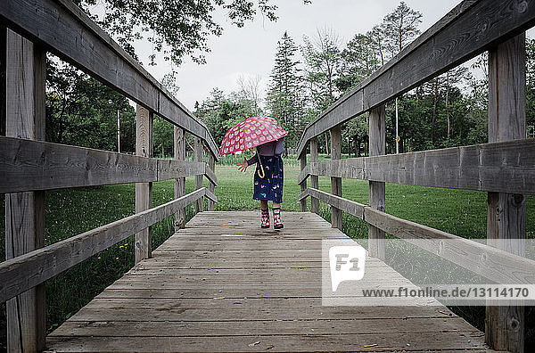 Mädchen mit Regenschirm geht während der Regenzeit auf einem Steg im Park