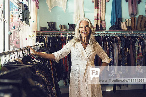 Porträt einer selbstbewussten Besitzerin lächelnd am Kleiderständer im Laden
