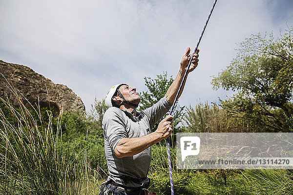 Mature man holding climbing rope on field