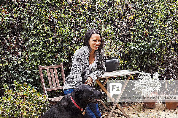 Smiling woman sitting on chair by Labrador Retriever at backyard
