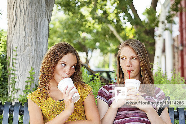 Freunde genießen ein Getränk  während sie auf einer Parkbank sitzen