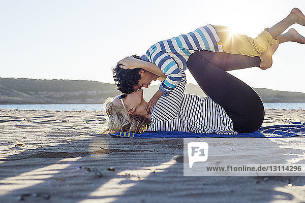 Seitenansicht einer liebenden Mutter  die ihren Sohn küsst  während er am Strand liegt