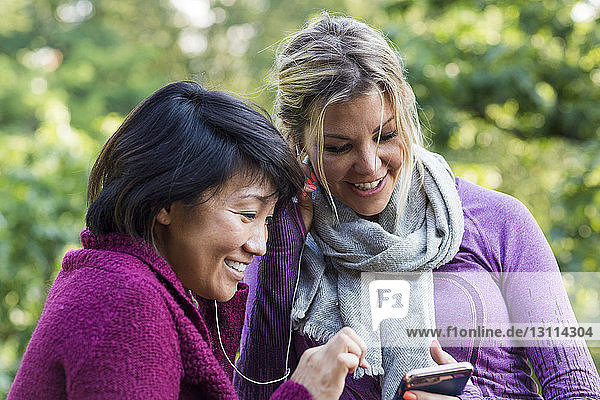 Happy female friends listening music while using smart phone at park