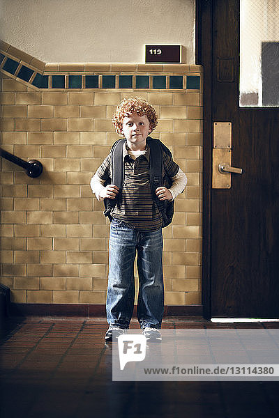 Porträt eines Jungen  der einen Rucksack trägt  während er vor dem Klassenzimmer steht