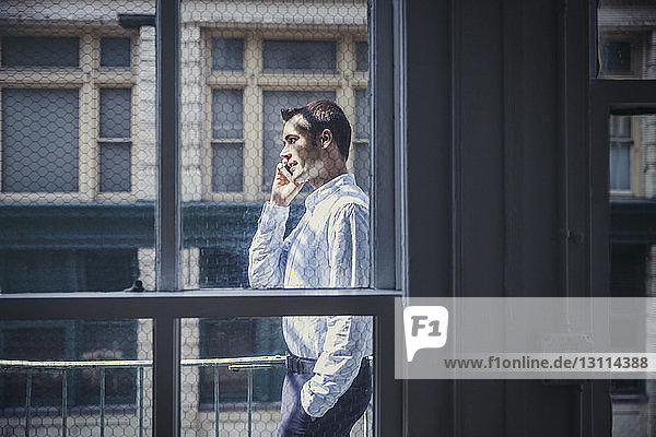 Seitenansicht eines Geschäftsmannes  der ein Smartphone benutzt  durch ein Fenster gesehen