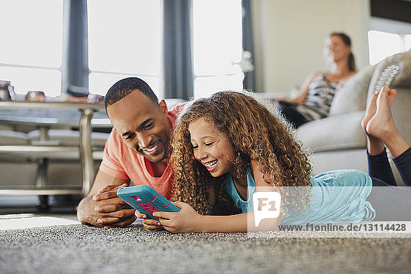 Glückliche Vater und Tochter spielen zu Hause auf dem Boden liegend ein Handheld-Spiel