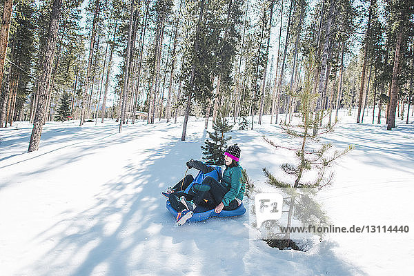 High angle view of mother and son sliding on snow covered field against trees