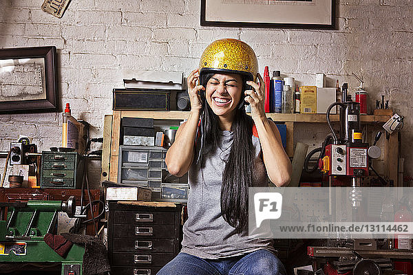 Cheerful female owner wearing helmet in auto repair shop