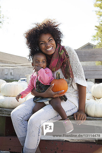 Happy mother holding pumpkin while sitting with daughter on table