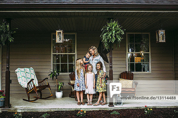 Glückliche Mutter mit Töchtern  die auf der Veranda vor dem Haus stehen