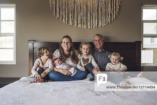 Portrait of happy parents with daughters sitting on bed at home