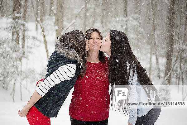Töchter küssen Mutter  während sie im Winter im Wald stehen