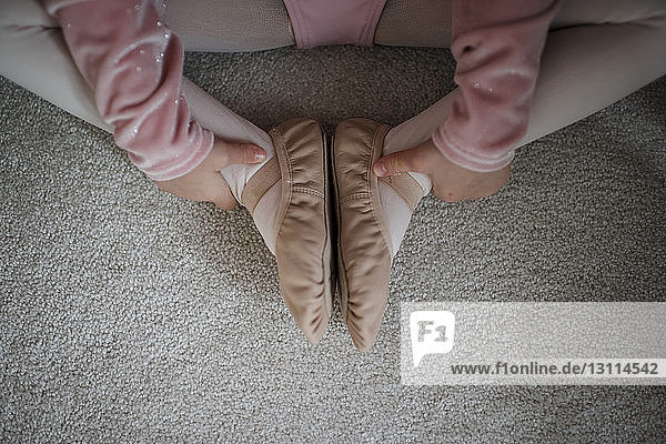Low section of girl in ballet costume sitting on rug at home