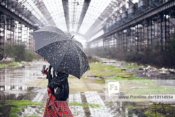 Woman carrying umbrella walking on field during snowfall