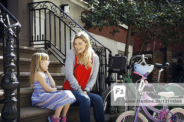Glückliche Mutter und Tochter unterhalten sich auf Stufen mit im Vordergrund geparkten Fahrrädern