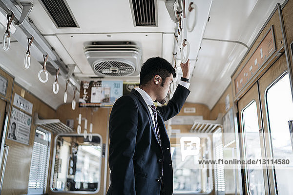 Side view of thoughtful young businessman looking through window while standing in train