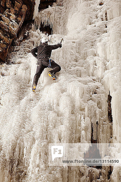 Mann klettert gefrorenen Wasserfall gegen Felsformation