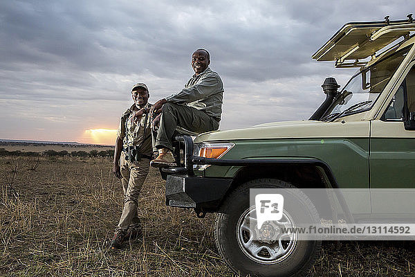 Portrait of male friends by off-road vehicle at Serengeti National Park during sunset