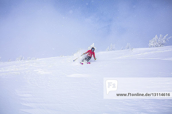 Frau fährt Ski auf schneebedeckter Landschaft gegen den Himmel