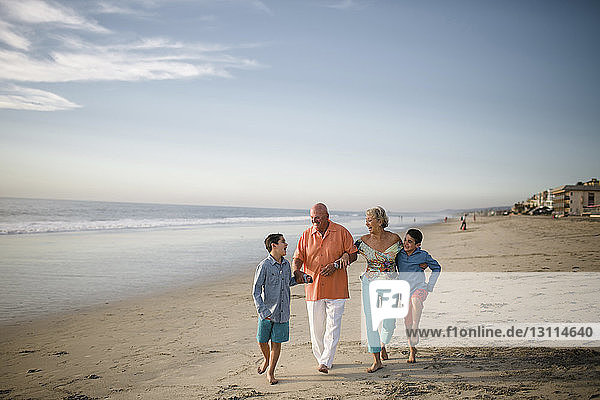 Glückliche Großeltern mit Enkeln  die am Strand gegen den Himmel laufen