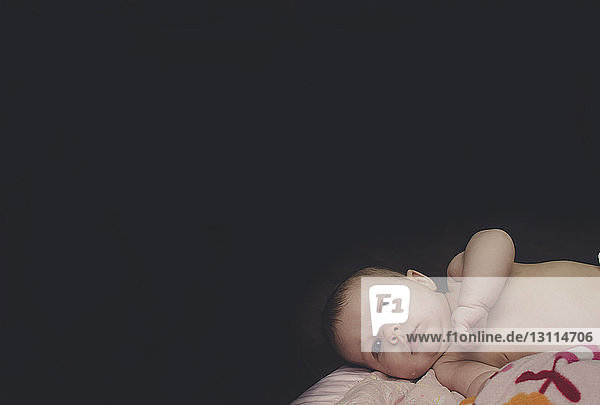 Porträt eines süßen  auf dem Bett liegenden Mädchens vor schwarzem Hintergrund