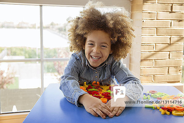Porträt eines lächelnden Mädchens  das zu Hause mit Spielzeug auf dem Tisch spielt