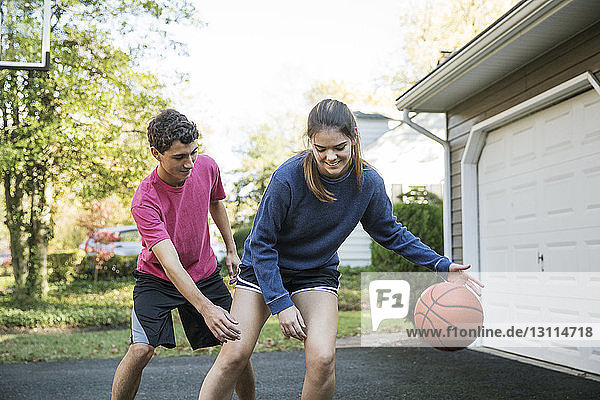 Happy brother and sister playing basketball at backyard
