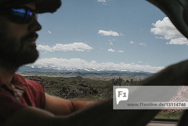 Mann im Auto mit Landschaft vor bewölktem Himmel im Hintergrund